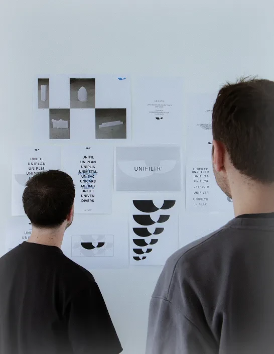 Two designers reviewing work pinned on a wall